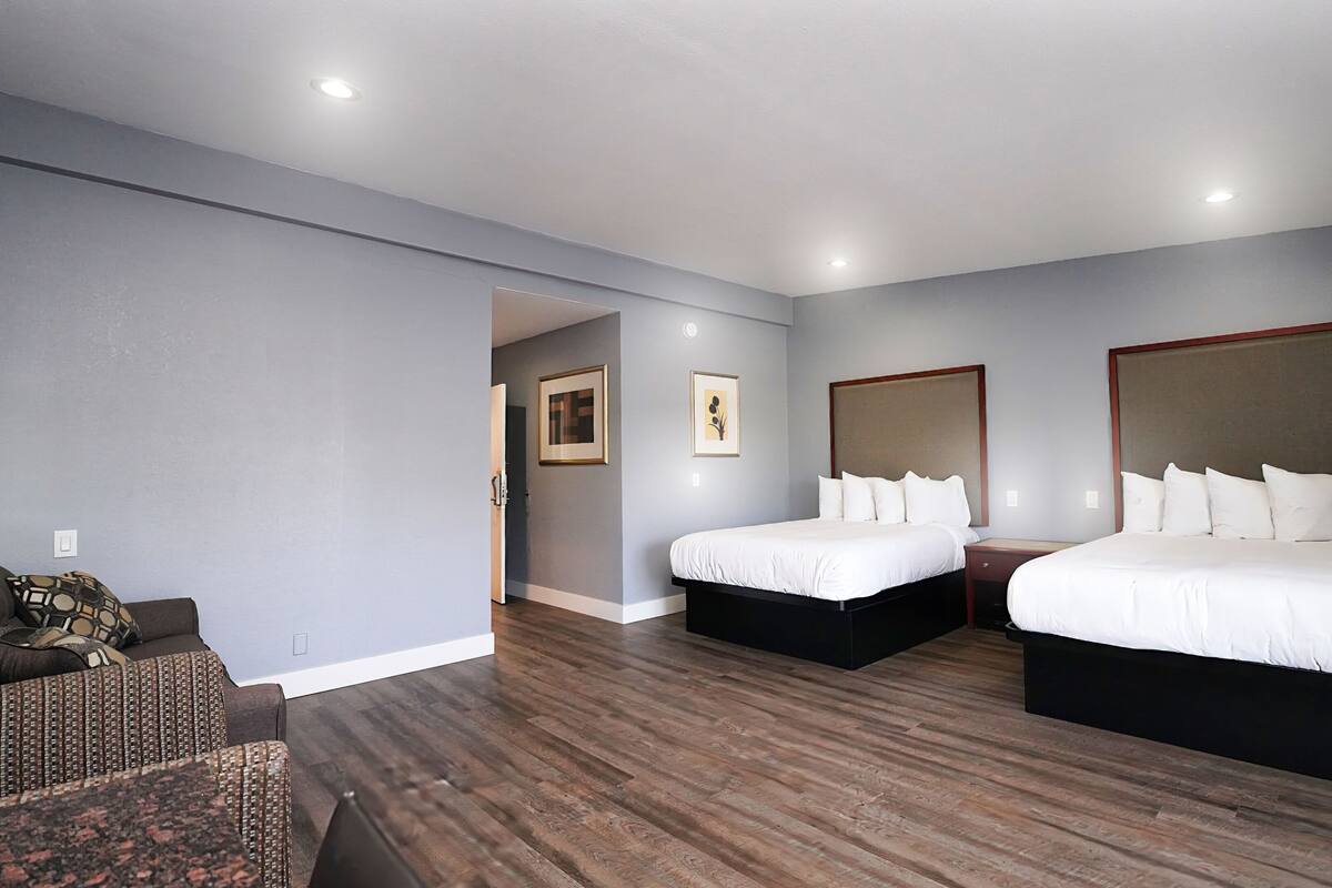 A hotel room with two beds, a sofa, and a wooden floor.