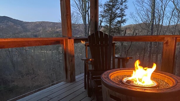 Una terraza de madera con un brasero y una silla, con vista a un paisaje montañoso.