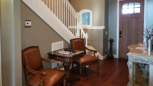 Una escalera con barandillas blancas, una mesa de madera con piezas de ajedrez y dos sillones de cuero.