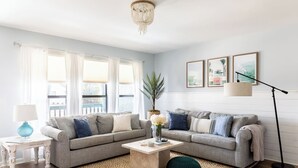 Een woonkamer met twee grijze banken, een bijzettafeltje, een lamp en een vloerlamp. Er hangen drie ingelijste foto’s aan de muur.