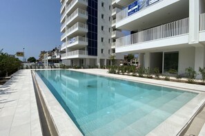 Un hôtel moderne doté d’une piscine, de nombreux balcons et offrant une vue sur un ciel dégagé.
