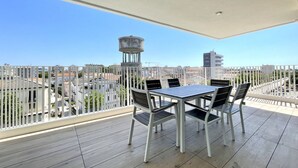 A balcony with a table and chairs, overlooking a cityscape with buildings and a water tower. - Appartamento Blu Homes 2 - Carraro Immobiliare Jesolo (Lido di Jesolo)
