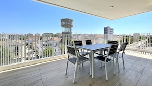 A balcony with a table and chairs, overlooking a cityscape with buildings and a water tower.