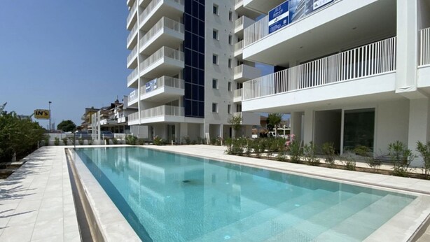A modern hotel with a swimming pool, multiple balconies, and a clear sky.