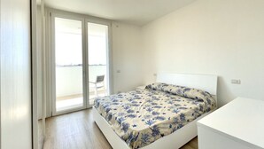 A bedroom with a bed, a white headboard, a small bedside table, and a sliding glass door leading to a balcony.