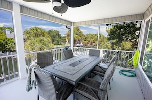 A covered balcony with a table and chairs, overlooking a body of water and trees.