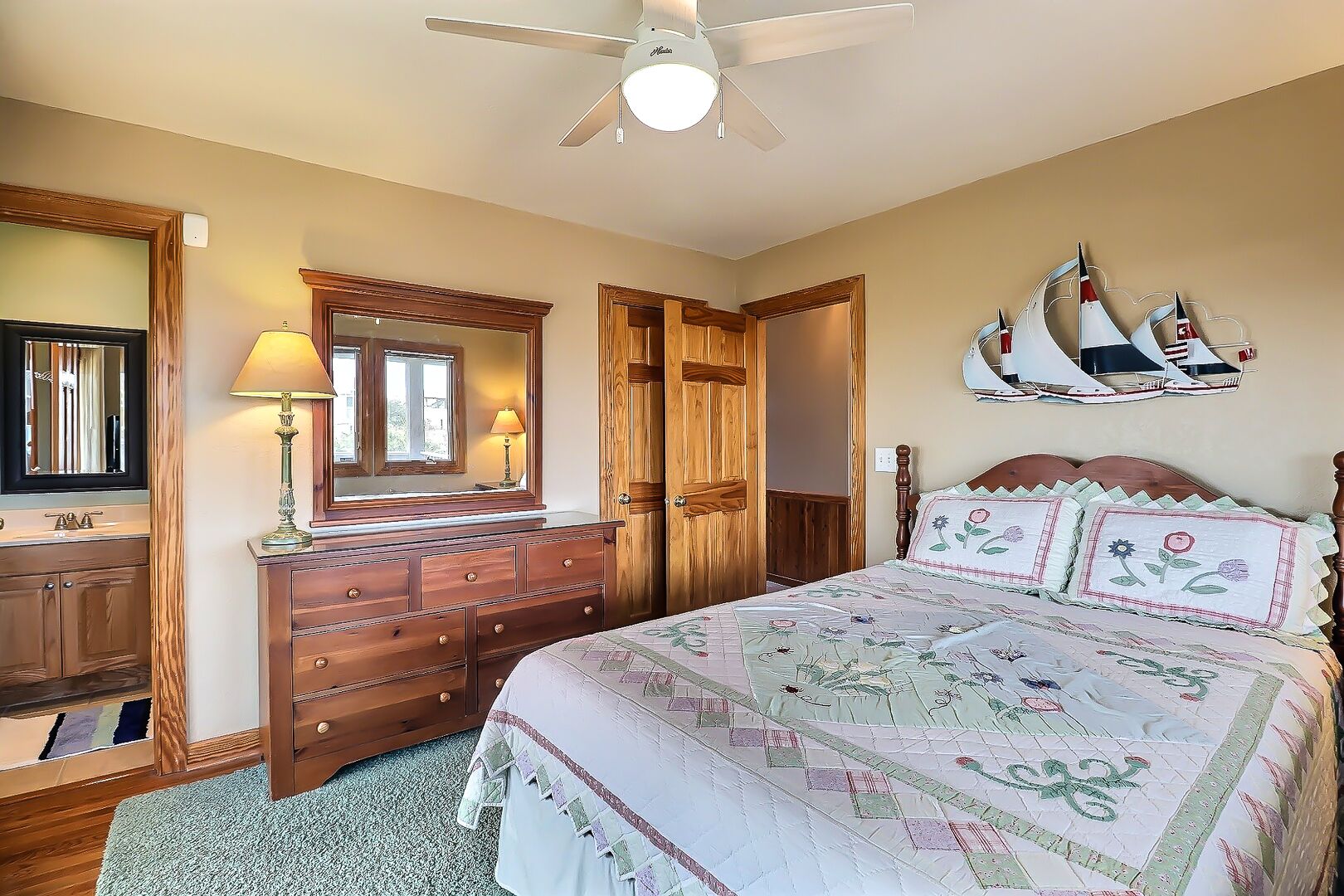A bedroom with a bed, dresser, mirror, and a ceiling fan.