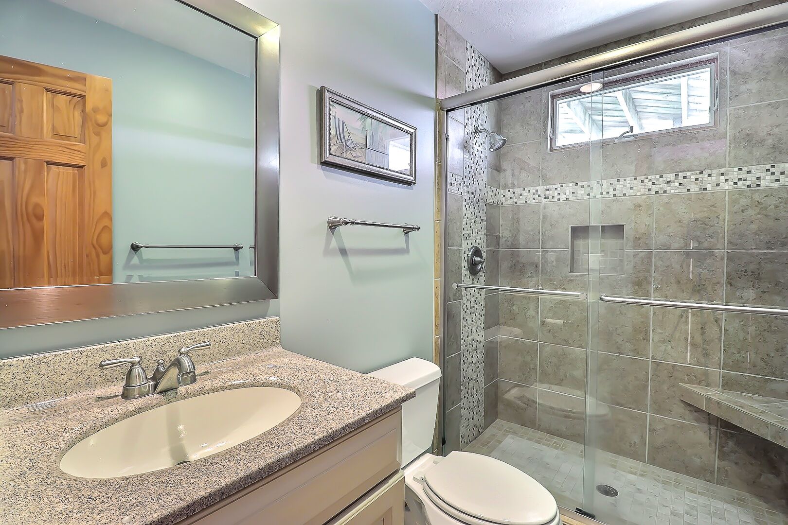 Un baño con lavamanos de encimera de granito, inodoro y ducha con cerramiento de vidrio.