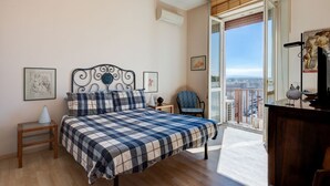 Un dormitorio con cama, una silla, una mesita de noche y vistas a la ciudad desde un balcón.