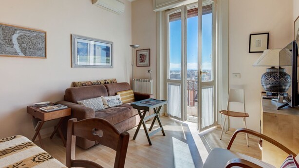 Un salón con un sofá, una mesa de centro, una silla, una lámpara y vistas a través de un ventanal.