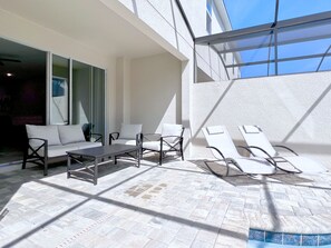 Une terrasse extérieure baignée de lumière, avec un canapé, des fauteuils et une table, offrant une vue sur le ciel à travers une structure en verre.