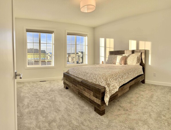 A bedroom with a large bed, two windows, and a view of buildings outside.