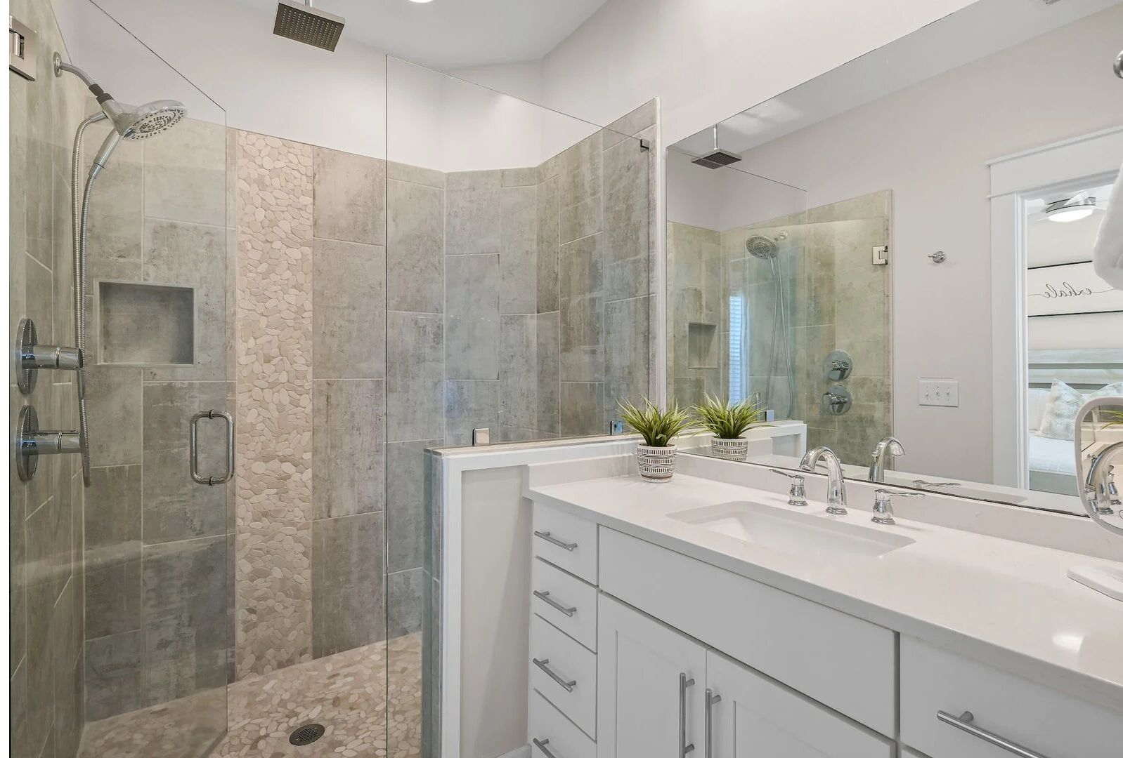 Un baño moderno con ducha de vidrio, un espejo grande y tocador doble.