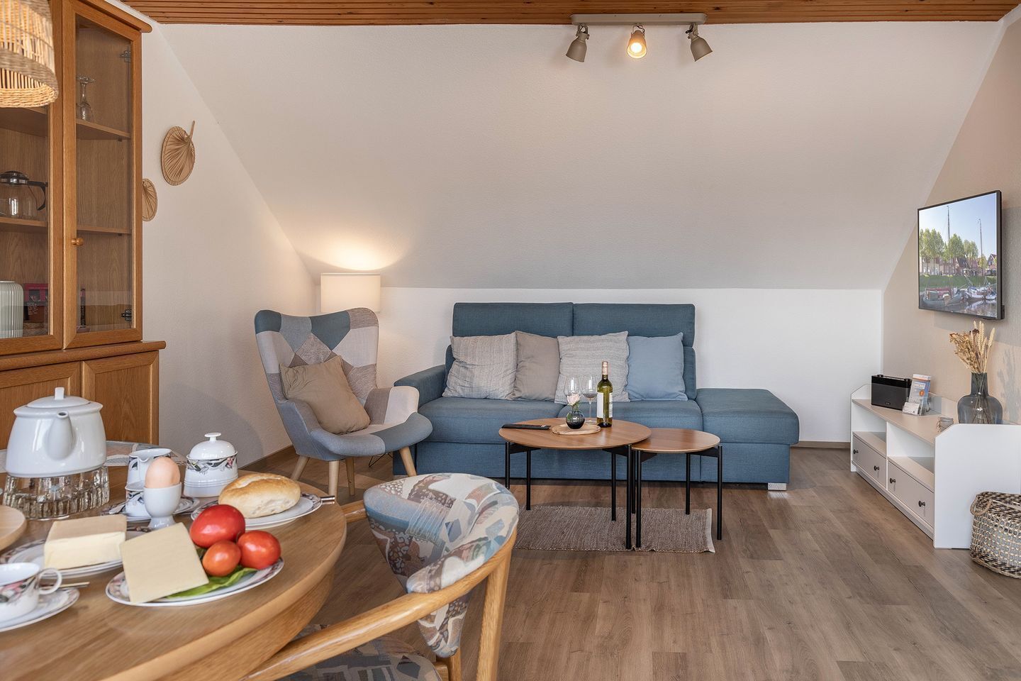 Una sala acogedora con un sofá azul, una mesa de comedor de madera con alimentos para el desayuno y un mueble de madera.