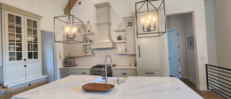 A modern kitchen with white cabinetry, a large island with bar stools, pendant lighting, and a visible stove.