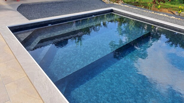 Ein rechteckiger Swimmingpool mit klarem Wasser, umgeben von einer gefliesten Liegefläche und einem Kiesstreifen.