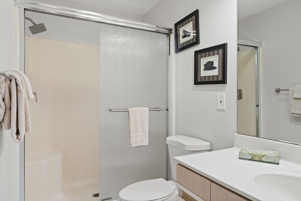 Une salle de bain avec une douche à parois de verre, des toilettes, un lavabo avec un miroir et deux tableaux encadrés au mur.