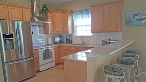 A kitchen with wooden cabinets, a stainless steel refrigerator, a stove, a sink, and bar stools.