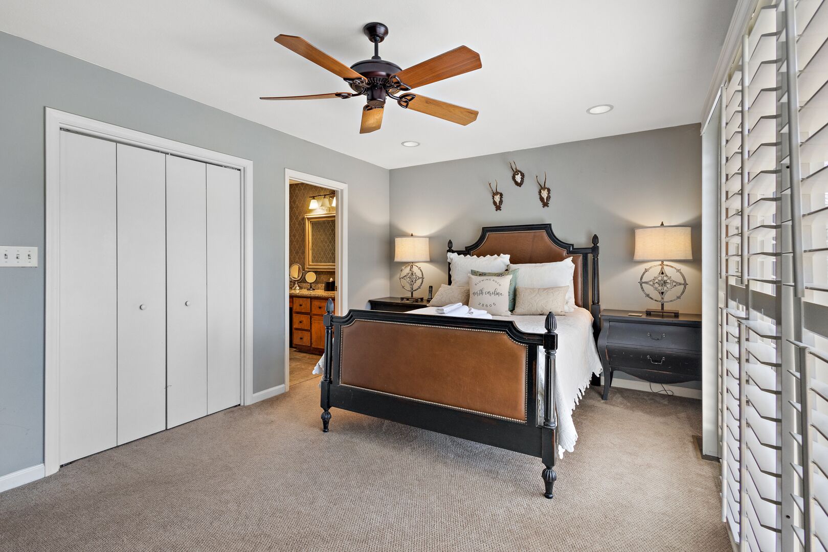 A bedroom with a bed, a ceiling fan, a nightstand, and a wall-mounted lamp.