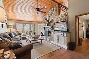 A cozy living room with a stone fireplace, a television, and a wooden ceiling fan. - Blue Ridge Parkway Lodge (Blowing Rock)