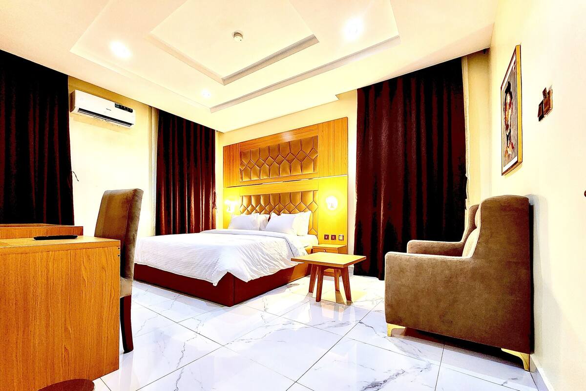 A hotel room with a large bed, a wooden desk, a chair, and a small table.