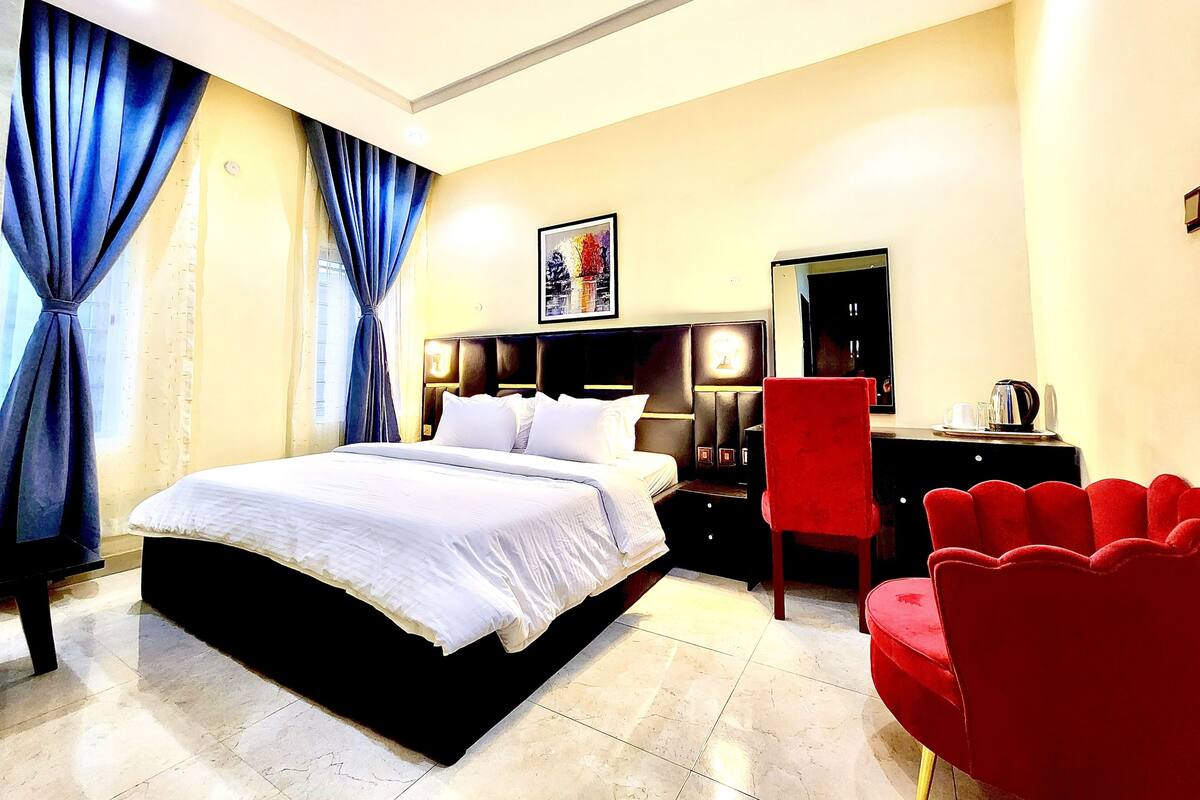 A hotel room with a large bed, a desk with a chair, a mirror, and a painting on the wall.