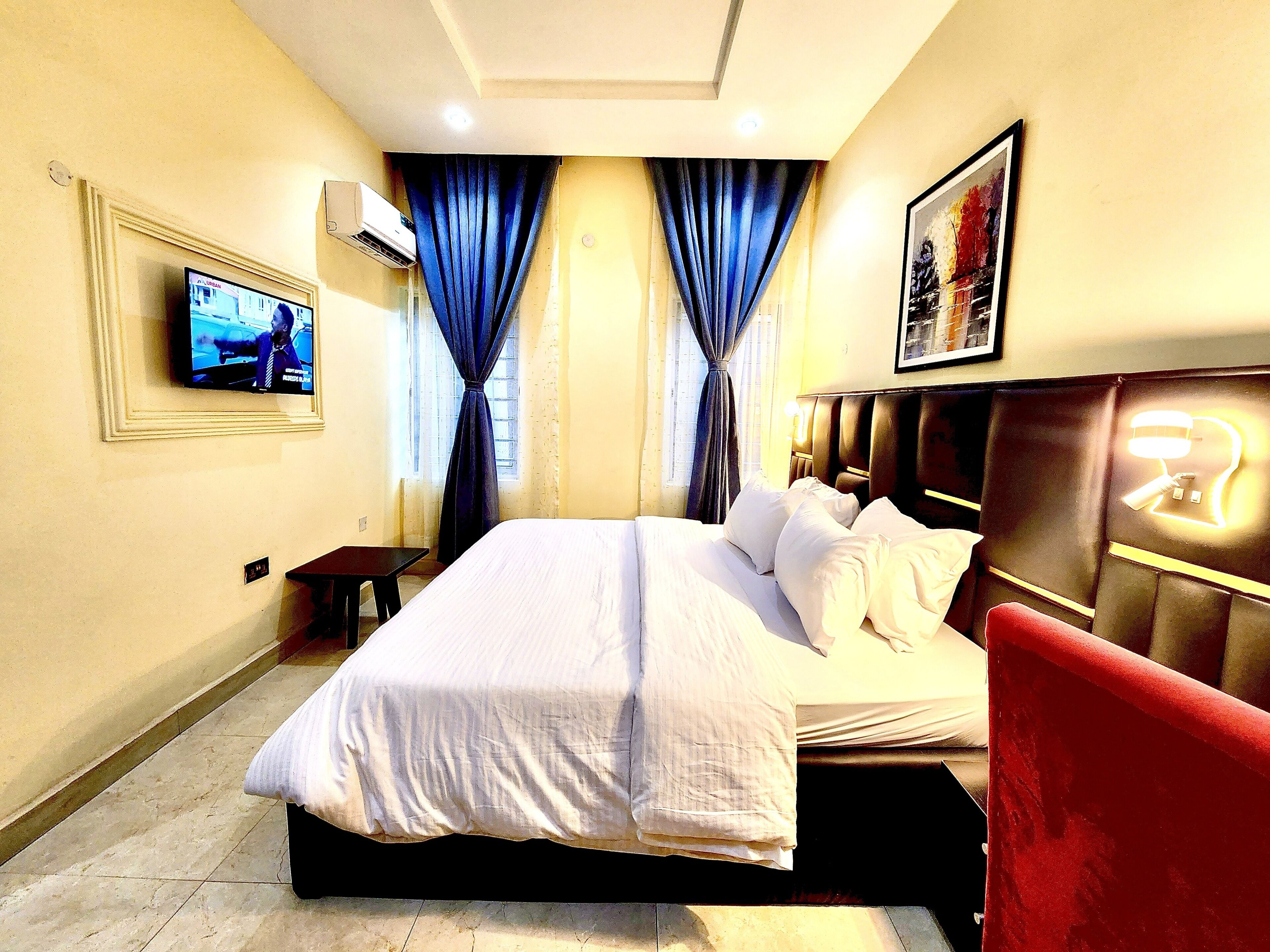 A hotel room with a bed, a TV, a desk, and a red chair.