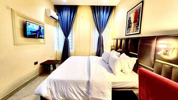 A hotel room with a bed, a TV, a desk, and a red chair.