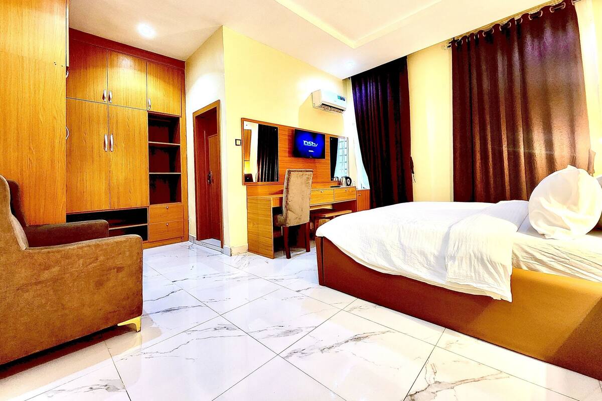 A hotel room with a bed, a desk, a chair, and a wardrobe.