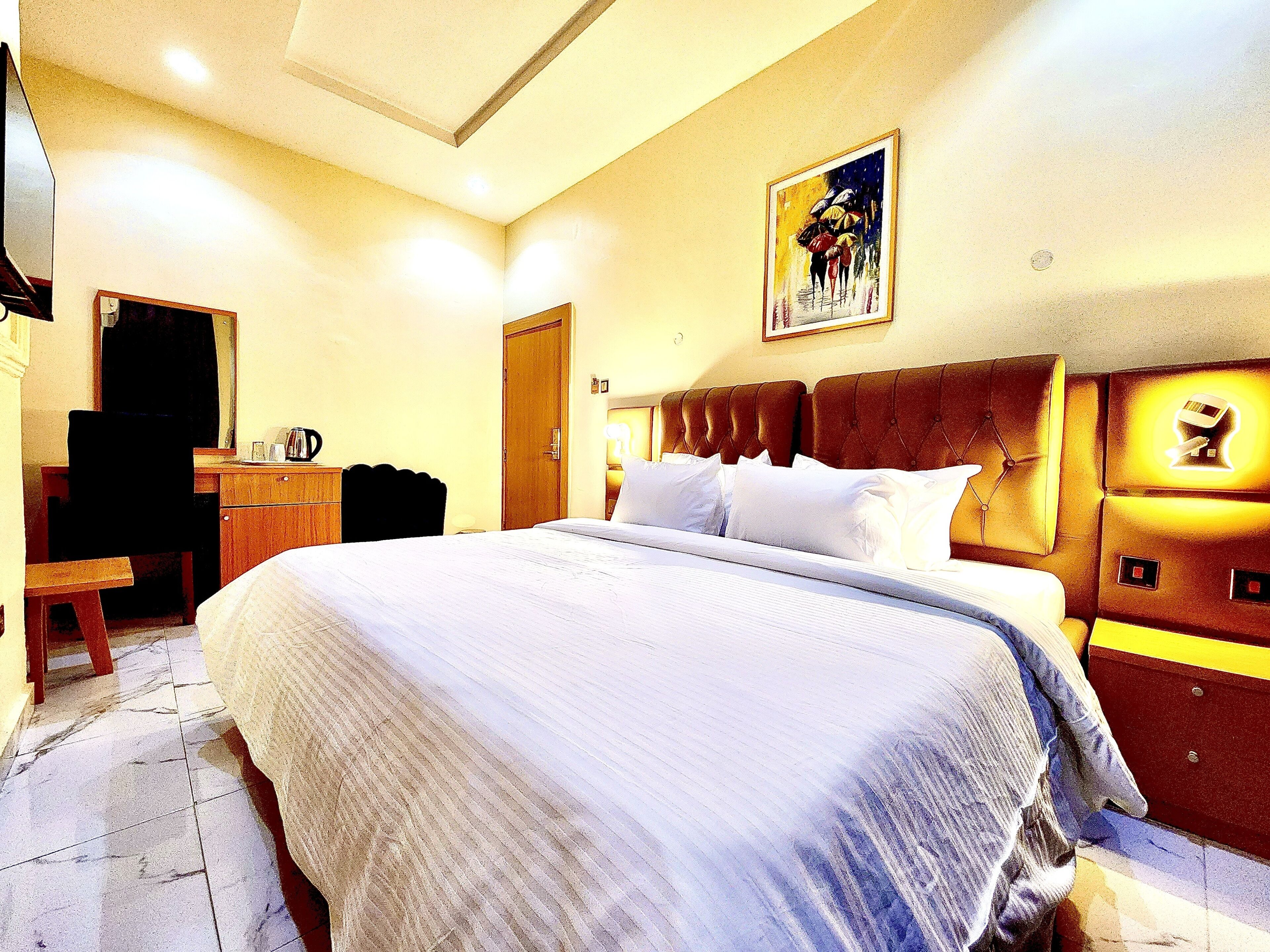 A hotel room with a large bed, a desk, a chair, and a door.