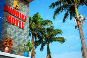 Un letrero de hotel con el nombre 'BUDDIEZ HOTEL' y una palmera al frente.