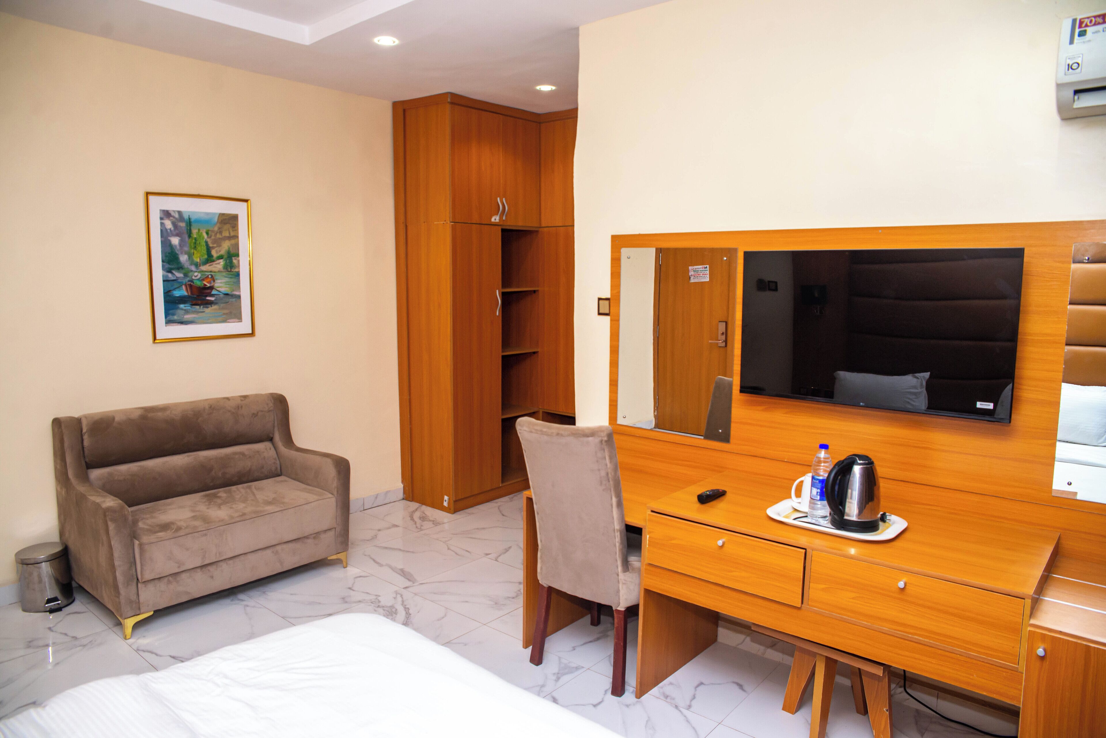 A hotel room with a bed, a wooden desk with a mirror, a brown sofa, a chair, and a small trash bin.