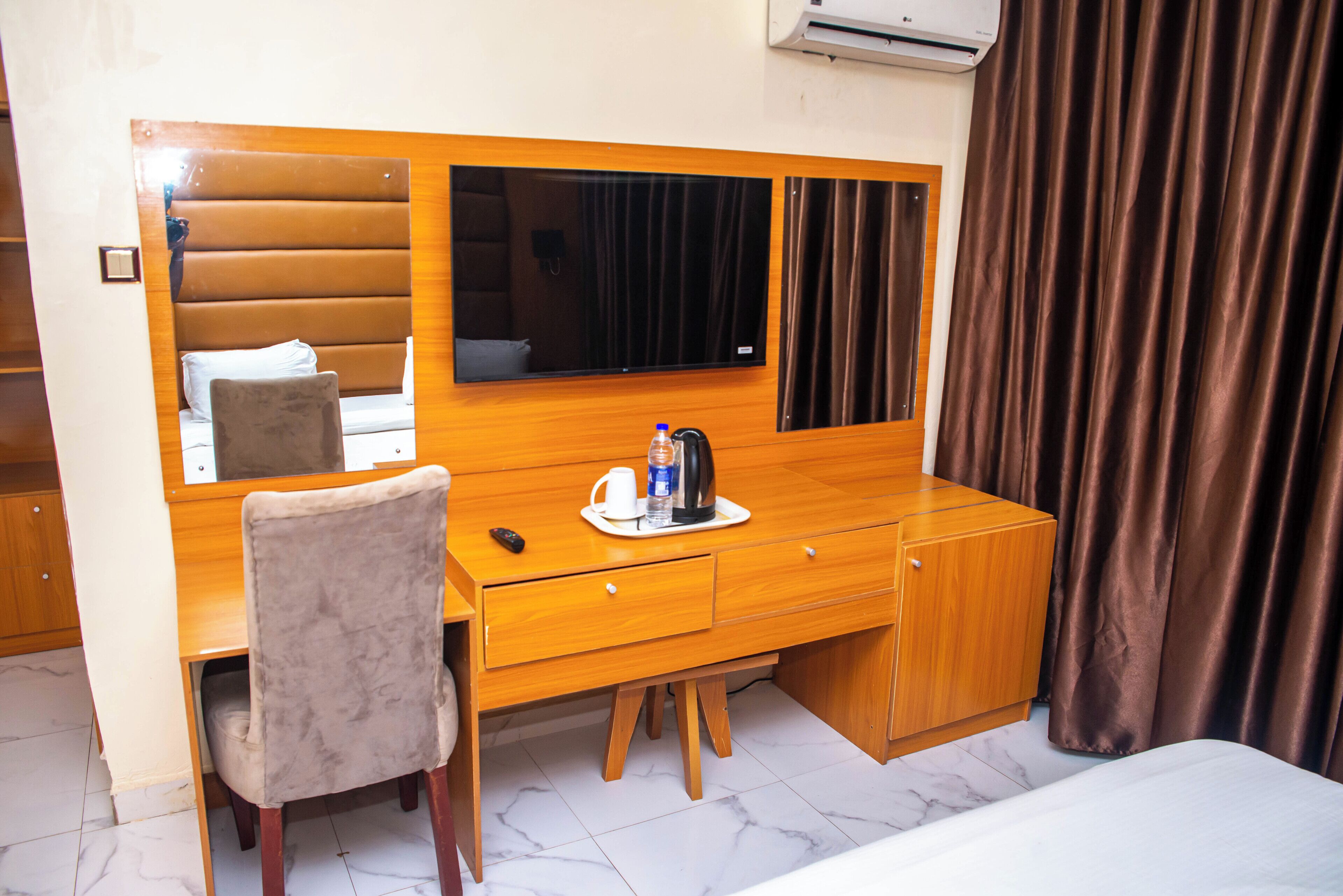 A hotel room with a wooden desk, a chair, a bed, a television, and a window with curtains.