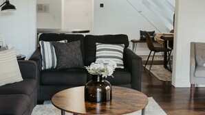 A modern living room with a dark sofa, a round coffee table, and a ceiling fan. - Lakefront Chalet - Dog Friendly w/ Hot Tub, Firepit and Kayaks (Six Lakes)