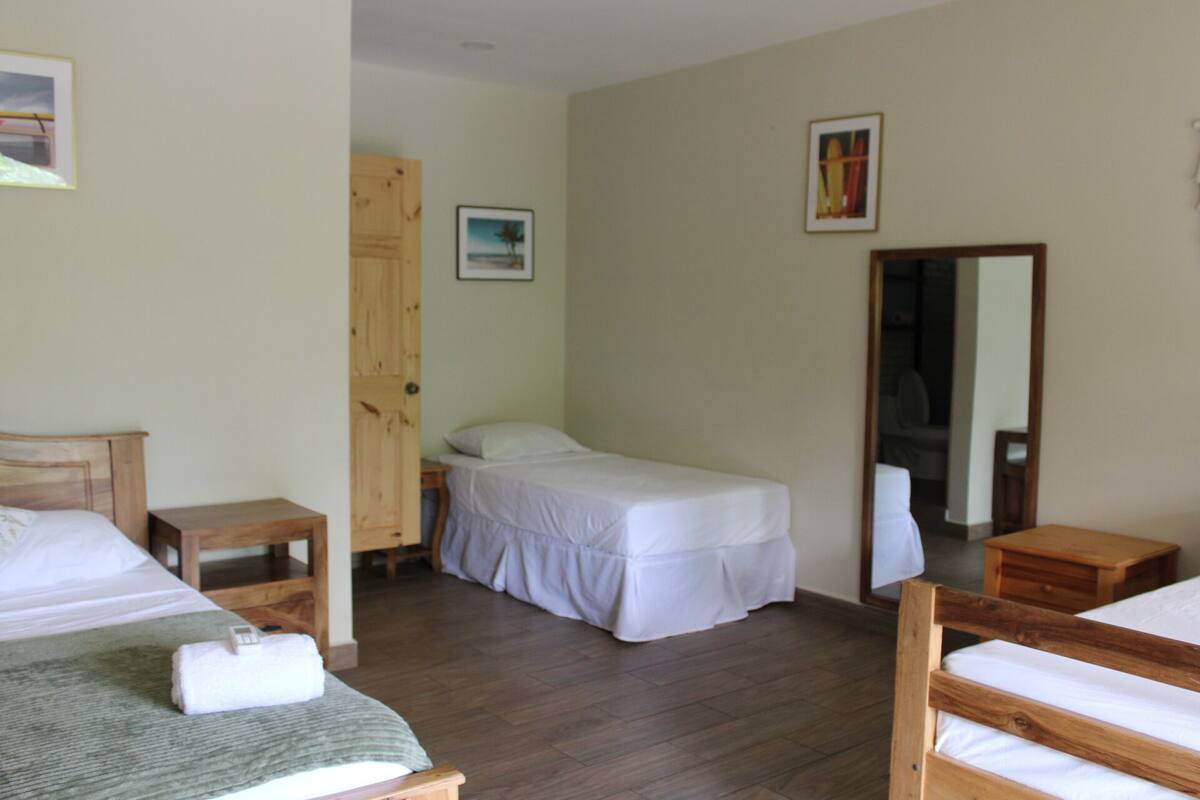 A room with two beds, a wooden door, a small bedside table, and a mirror.