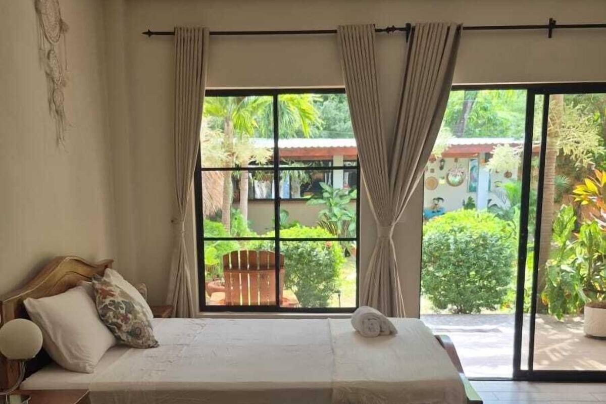 A bedroom with a large bed, wooden floor, and a view of a garden through a sliding glass door.