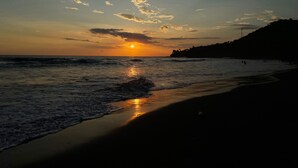 Una playa al atardecer con olas, cielo despejado y una colina distante.