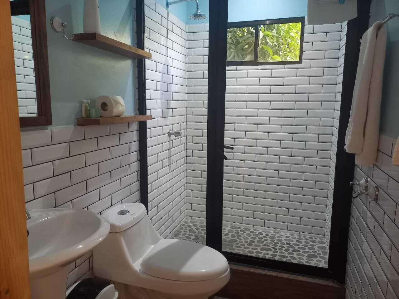 Een badkamer met witte betegelde wanden, een douche met glazen deur, een toilet en een wastafel.