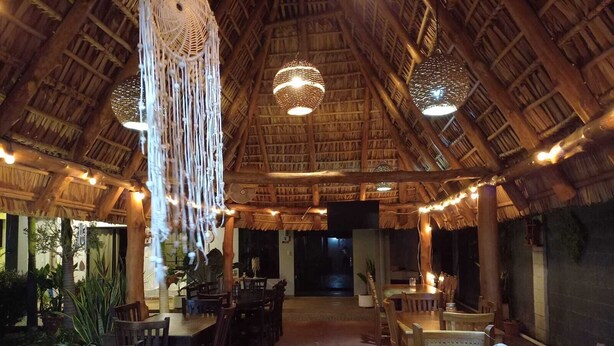 Un restaurante con techos de paja, mesas de madera y decoraciones de macramé colgantes.