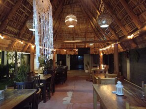 Un restaurant doté d’un toit de chaume, de tables en bois et de décorations en macramé suspendues.