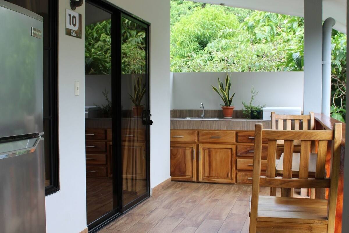 A modern kitchen with wooden cabinets, a stainless steel refrigerator, and a dining area with a wooden chair.