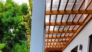 Un sendero conduce a un edificio con una pérgola de madera, rodeado de abundante follaje y una llamativa flor naranja.