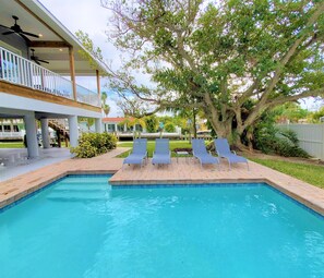 A swimming pool with lounge chairs, a covered deck, and a large tree.