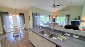 Una cocina moderna con una isla central, un comedor con mesa y sillas, y un amplio ventanal que proporciona luz natural.