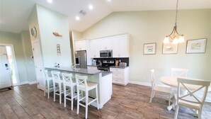 Una cocina amplia con una isla central, armarios blancos y un comedor con una mesa redonda y sillas.
