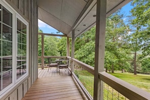 A covered porch with a wooden deck, a table with chairs, and a view of a wooded area.