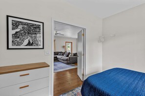 Une chambre à coucher avec un lit, une commode, une œuvre d’art encadrée et une vue sur le salon.