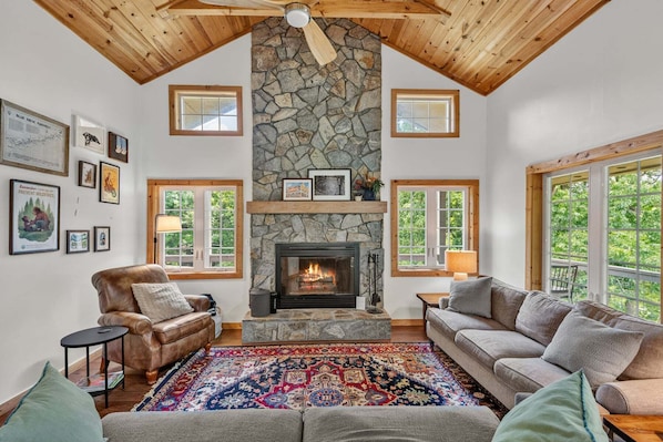 A cozy living room with a stone fireplace, leather armchairs, and a colorful rug.
