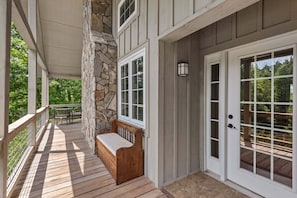 A covered porch with a stone wall, wooden bench, and a door with glass panels.
