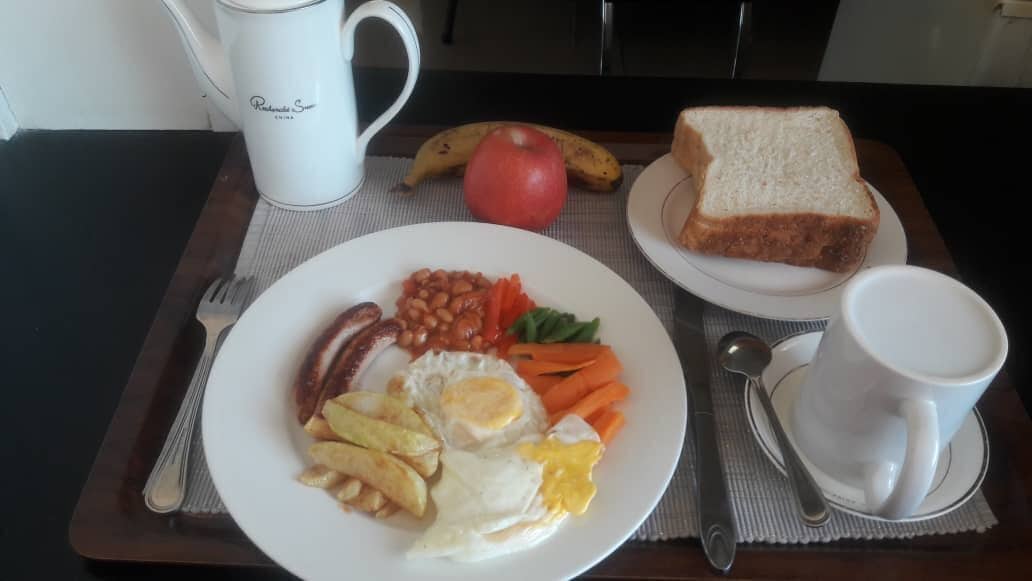 A breakfast tray with eggs, beans, fries, and toast, along with a banana, apple, and a cup of coffee.